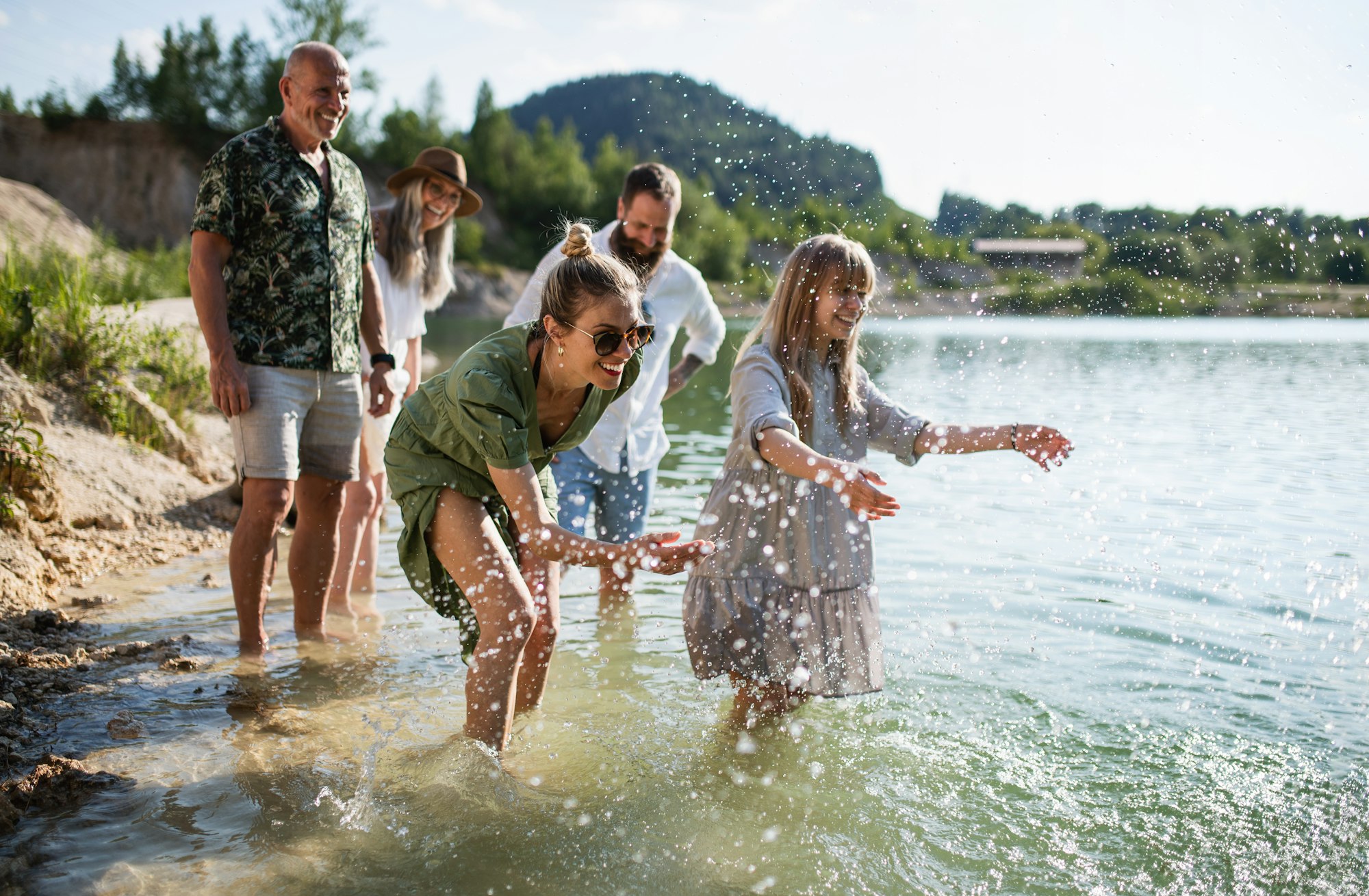 Happy multigeneration family on walk by lake on summer holiday, having fun in water
