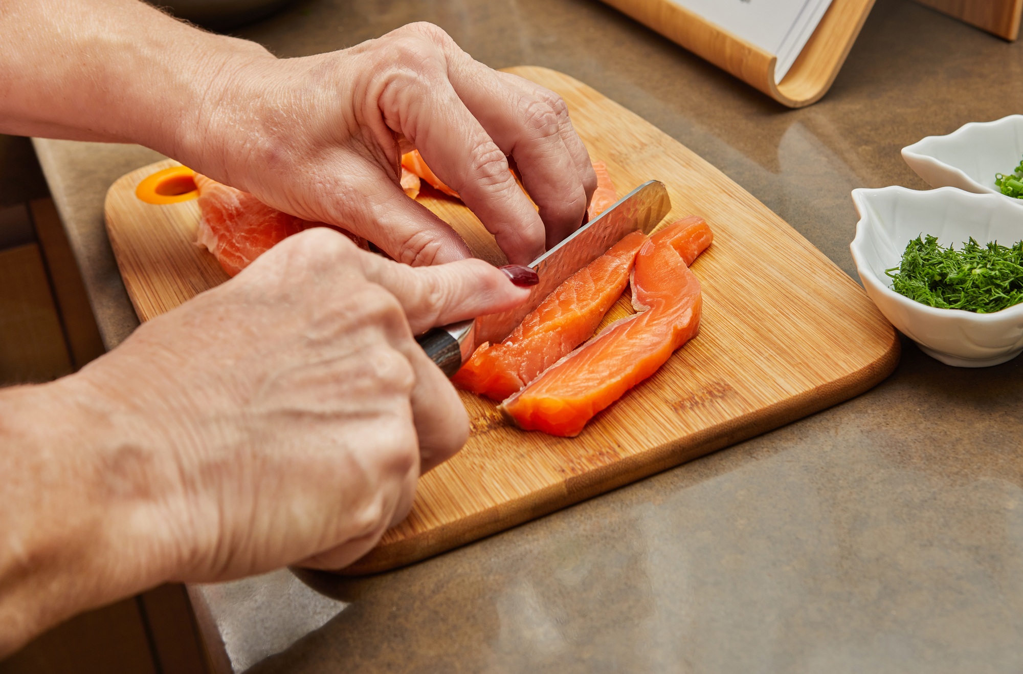 Chef cuts the salmon with knife into strips to prepare the dish according to the recipe